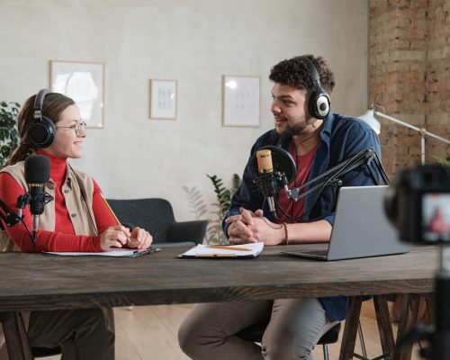 Man interviewing a woman at radio Young man in headphones interviewing a woman at the table during broadcasting at radio studio